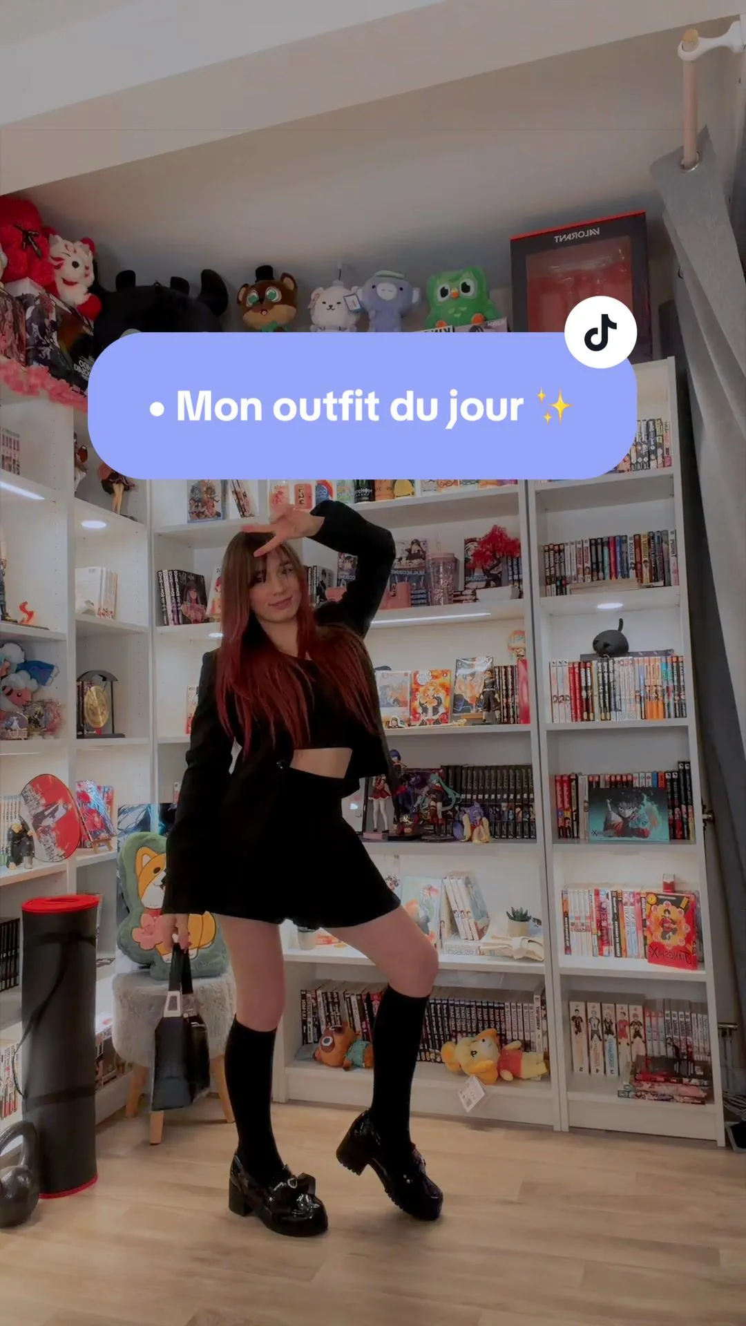 Natsumi présente une tenue noire devant sa collection de mangas